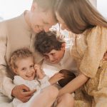 Cheerful family of four cuddling and smiling together in a bright, sunlit living room setting.